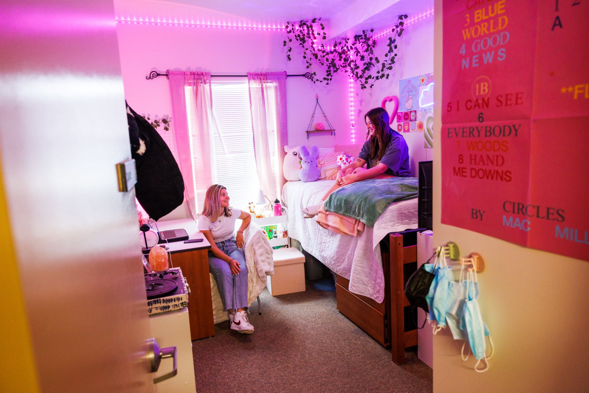 Two female students talking in a dorm room; one is on a bunk bed, and the other is sitting at a desk